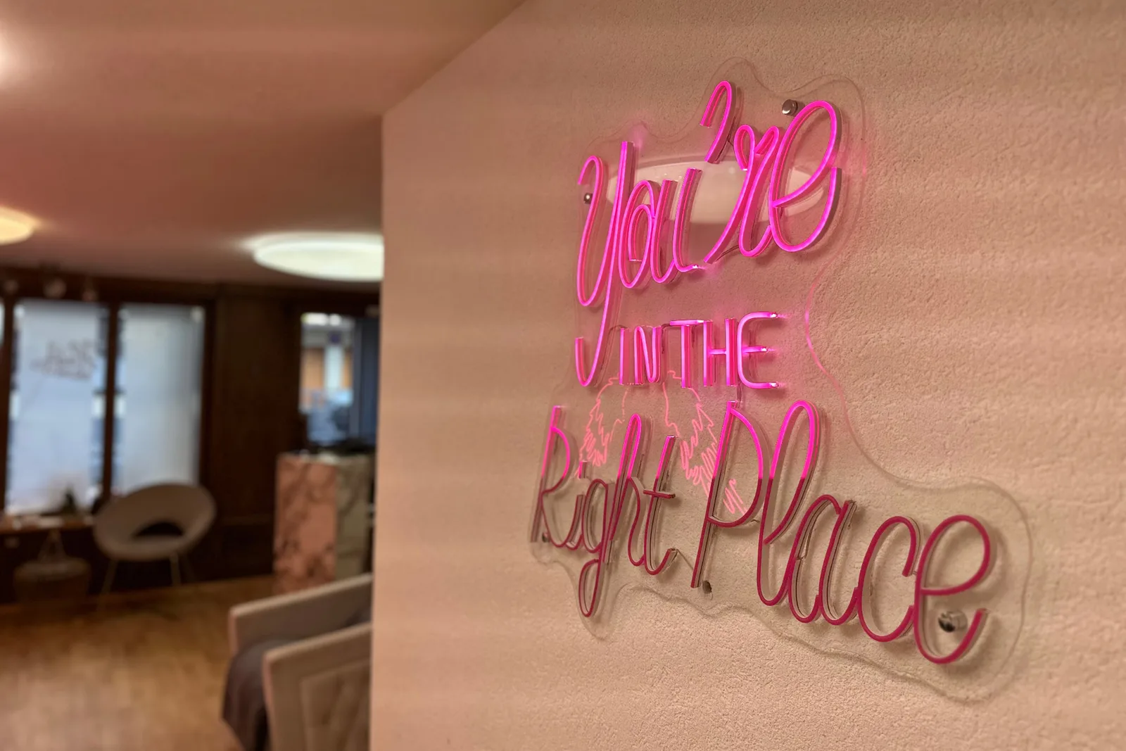 Pinkes Neonschild an der Wand des Salons, dahinter unscharf der Wartebereich