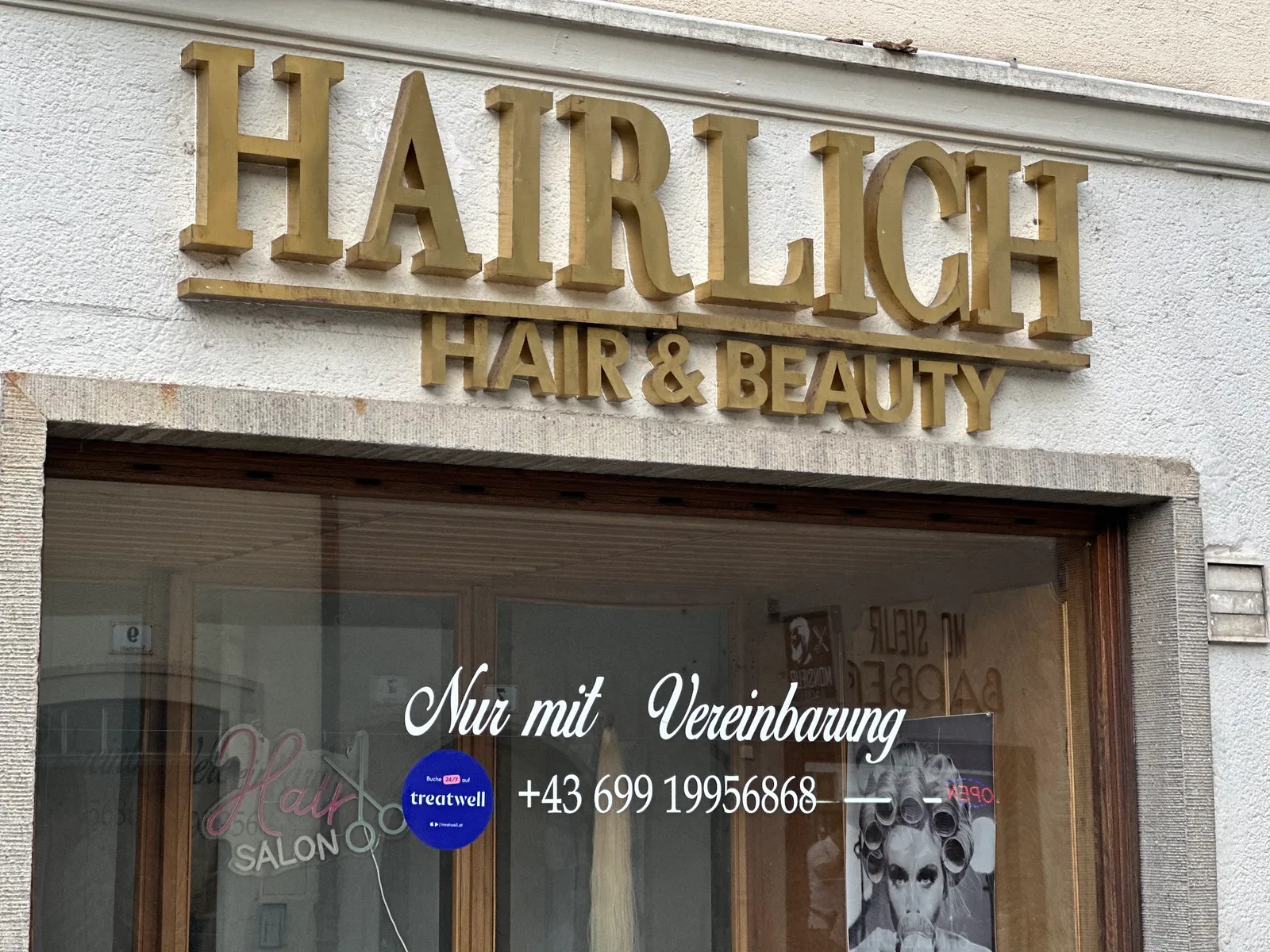 Fassade des Salons mit den goldenen Buchstaben HAIRLICH HAIR & BEAUTY über dem Schaufenster
