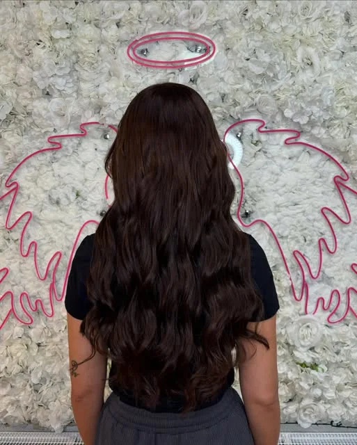 Lange dunkelbraune Wellen vor der Blütenwand mit dem Neon-Engelsflügel